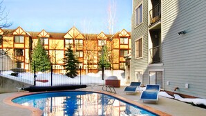 A swimming pool with lounge chairs, surrounded by a fence and trees, with buildings in the background. - Carriage House Condominiums by All Seasons Resort (Park City)