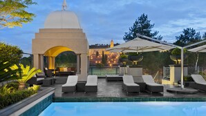 Un área junto a la piscina con sillones, una zona de estar cubierta y vistas a un edificio con cúpula.