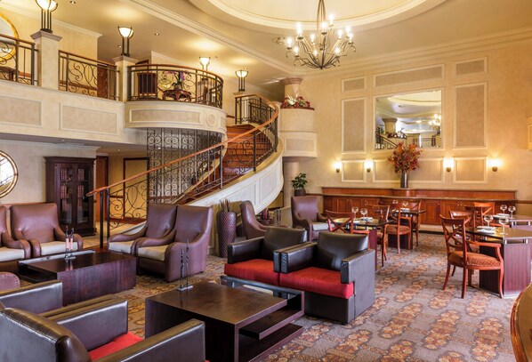 A spacious lobby with a grand staircase, leather seating, and a bar area.