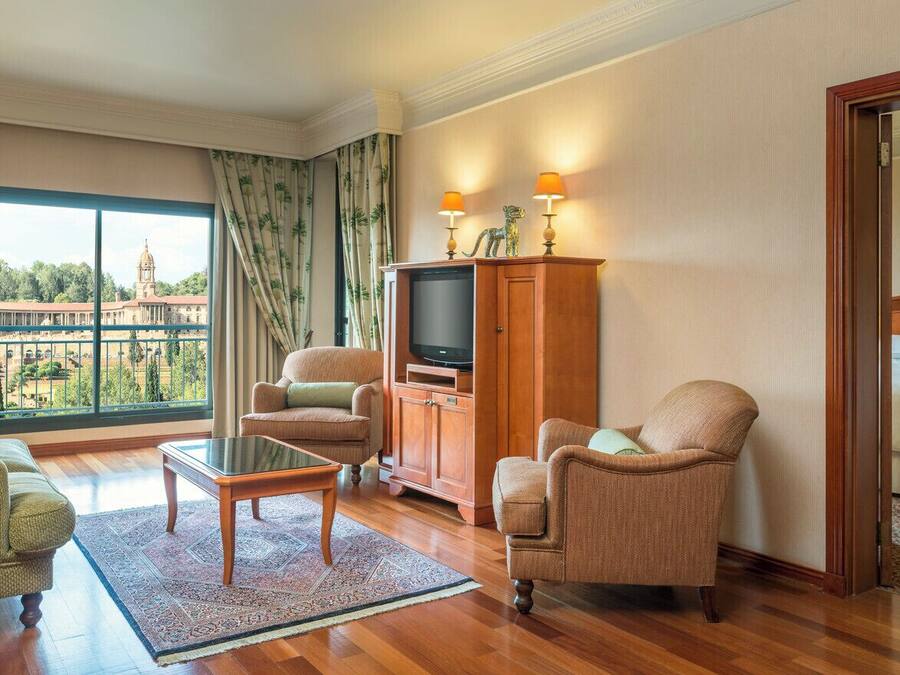 Habitación de hotel con un ventanal grande, televisor, dos sillones, un sofá, un armario de madera y una cama.