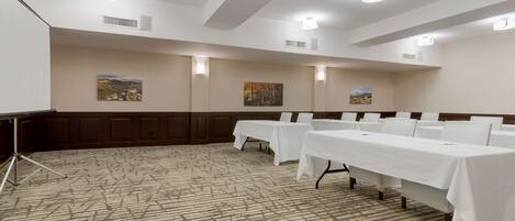 A conference room with a patterned carpet, white tables with chairs, and wall-mounted artwork.