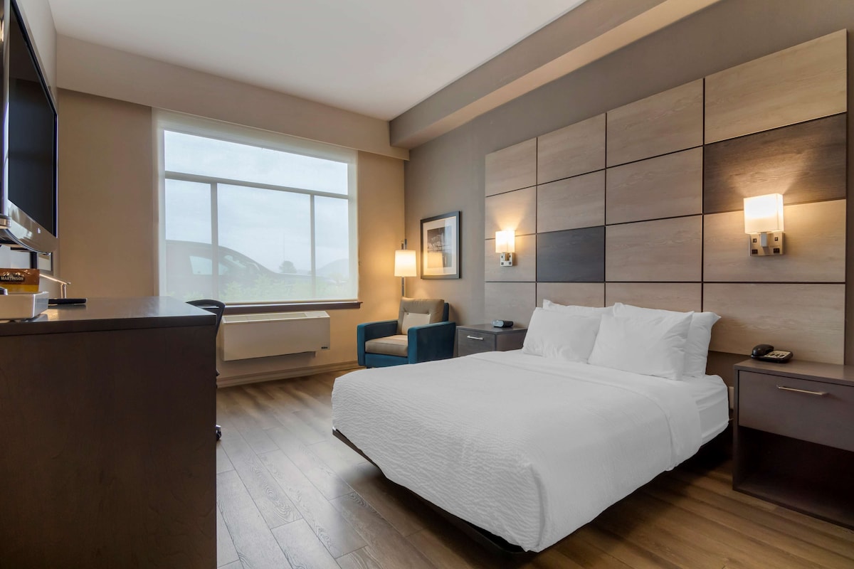 A modern hotel room with a large bed, a desk, a chair, and a window with a view.