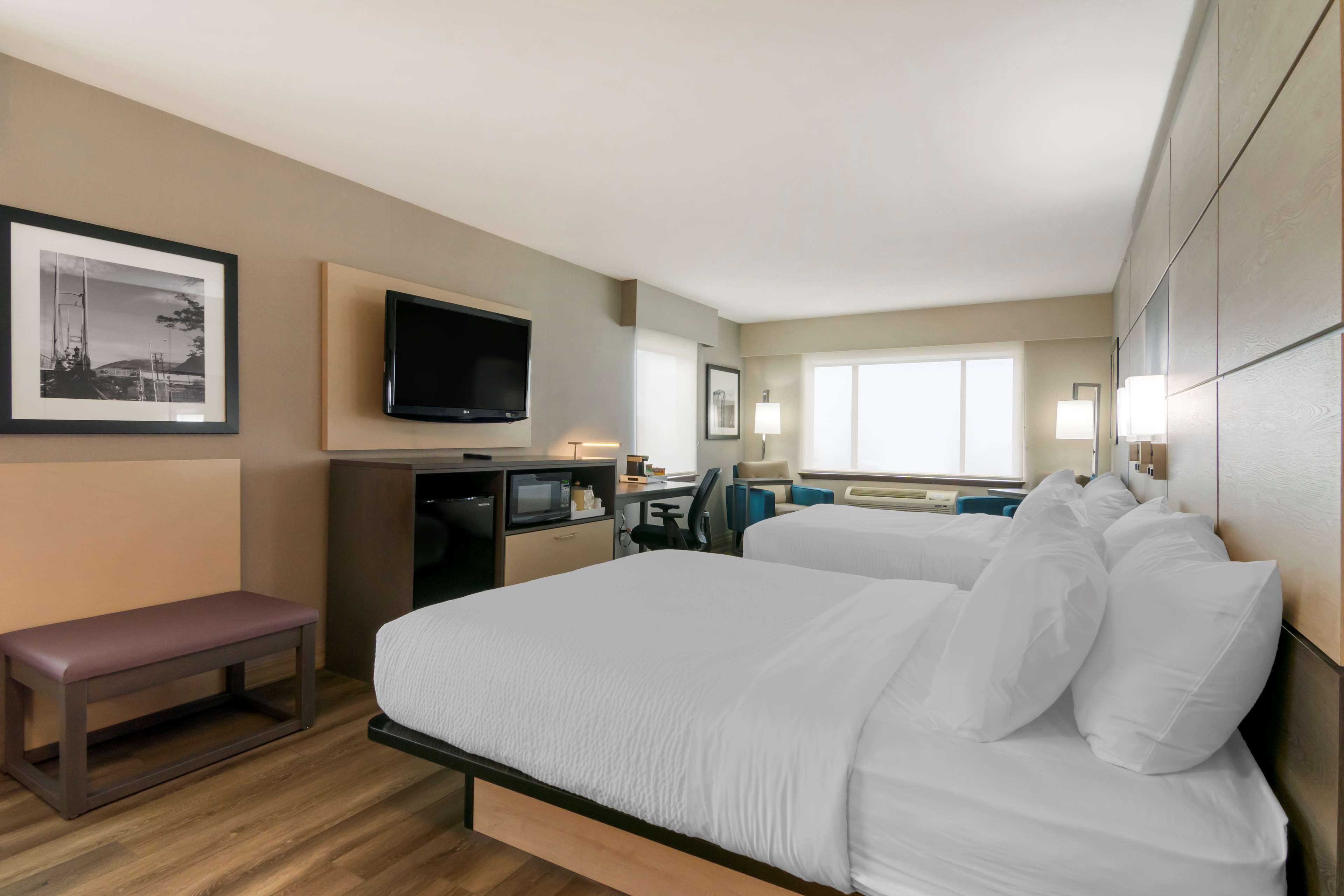 A hotel room with a bed, a desk, a television, and a bench.