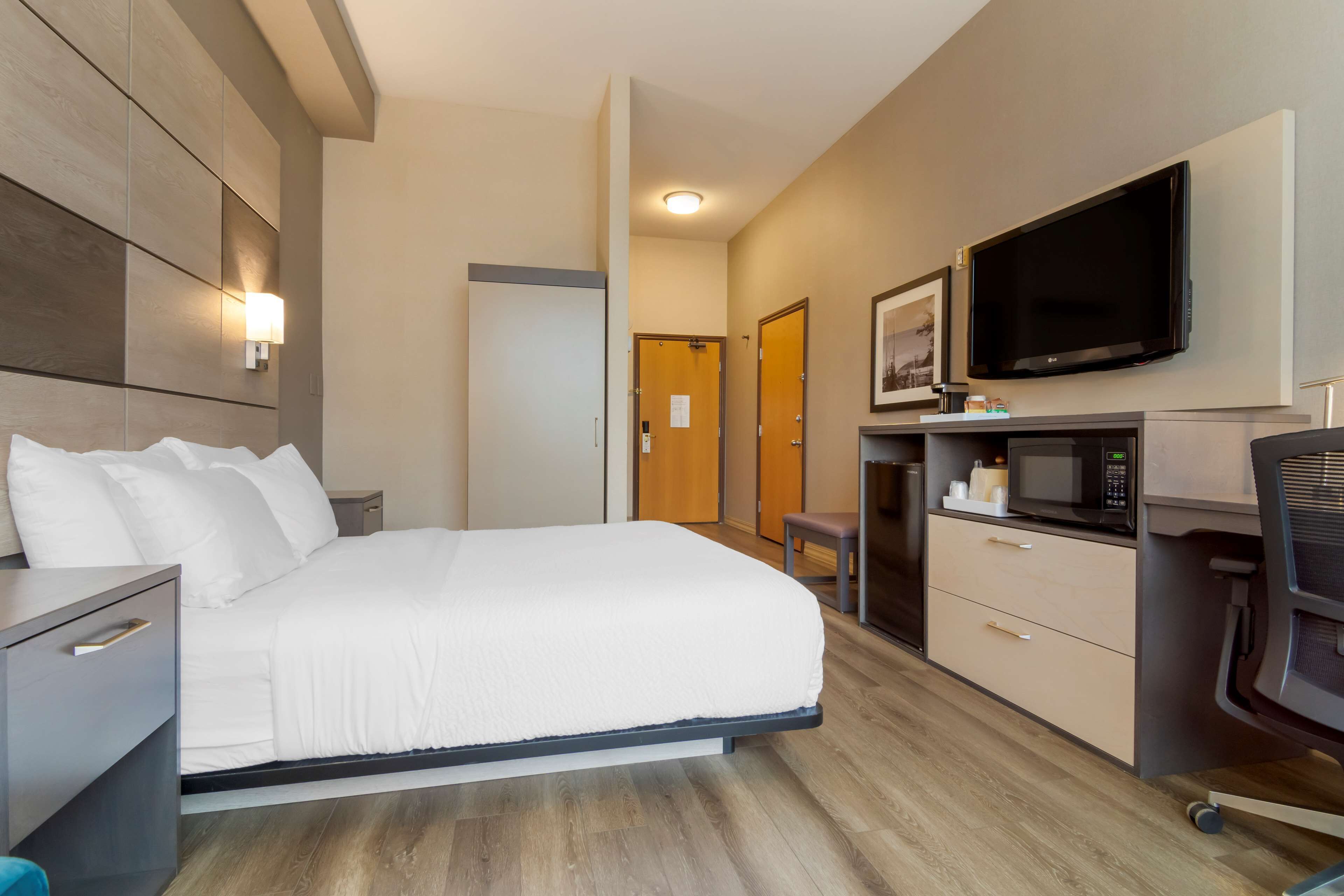 A hotel room with a bed, a desk with a chair, a TV, and a microwave.