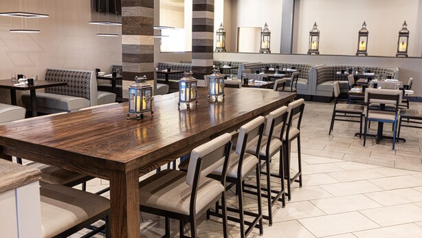 Un restaurante con una larga mesa de madera, asientos acolchados y faroles decorativos.