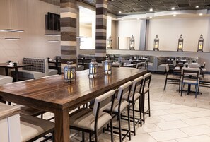 A restaurant with a long wooden table, cushioned seating, and decorative lanterns. - Holiday Inn St. Louis Arpt West-Earth City by IHG (Earth City)