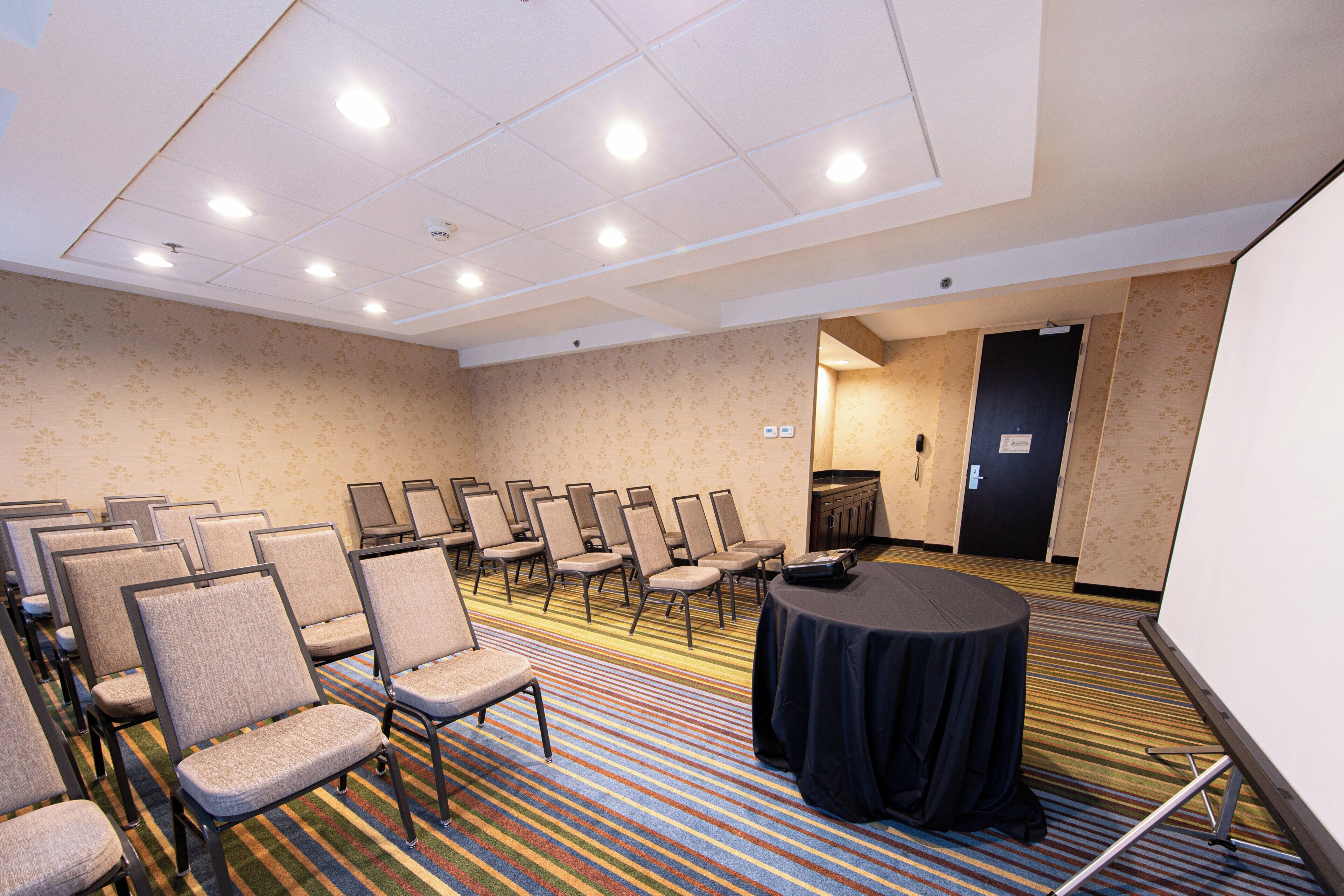 A conference room with rows of chairs, a projector screen, and a carpeted floor.