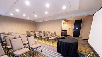 A conference room with rows of chairs, a projector screen, and a carpeted floor.