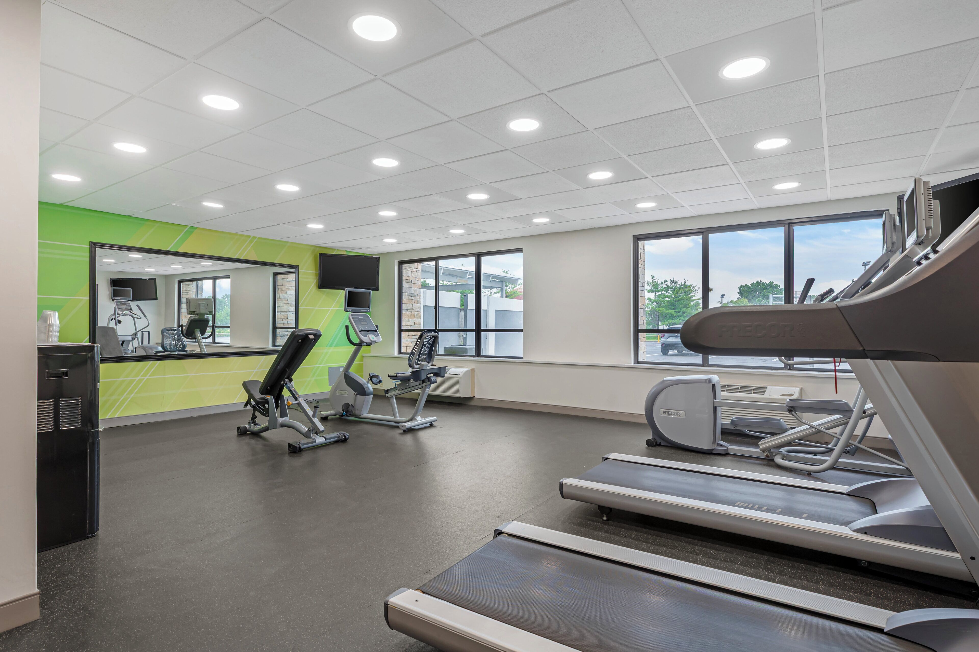A gym with exercise equipment, large windows, and a green accent wall.