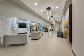 Een moderne hotellobby met een receptiebalie, een zithoek en een groot schilderij aan de muur.