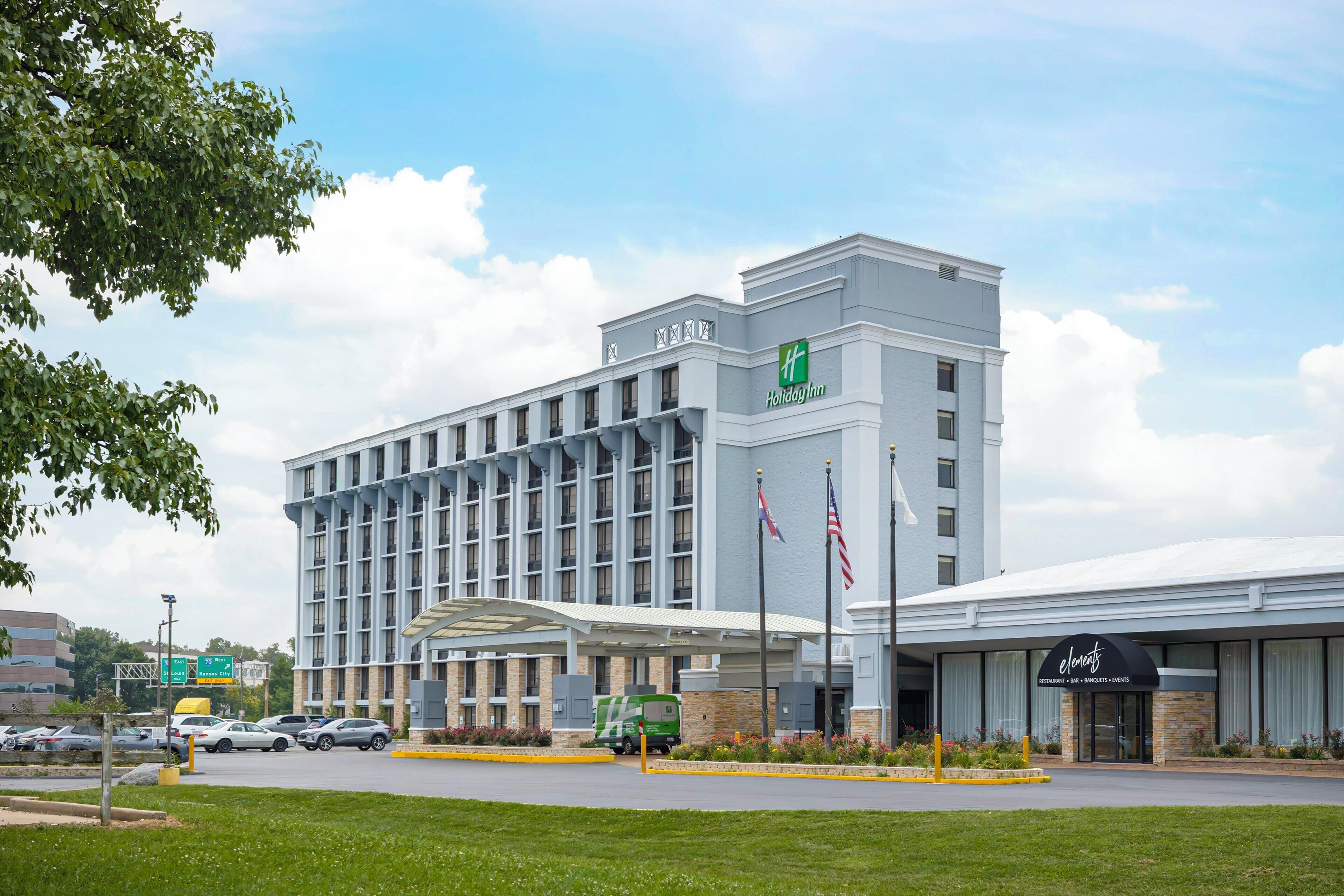 A Holiday Inn hotel with a modern design, featuring a large parking lot and a restaurant named 'Elements'.