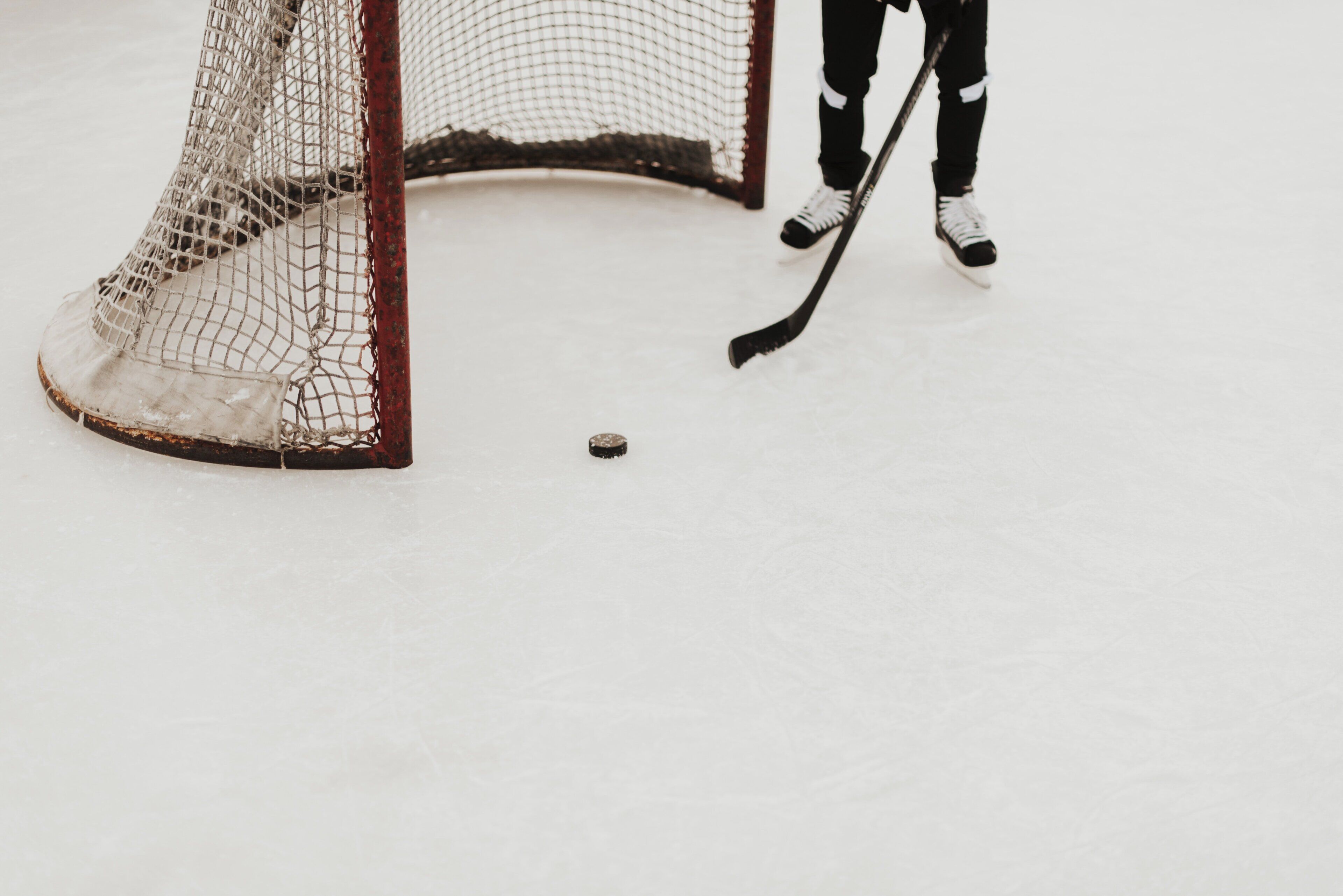 A hockey goal with netting and a puck on the ice.