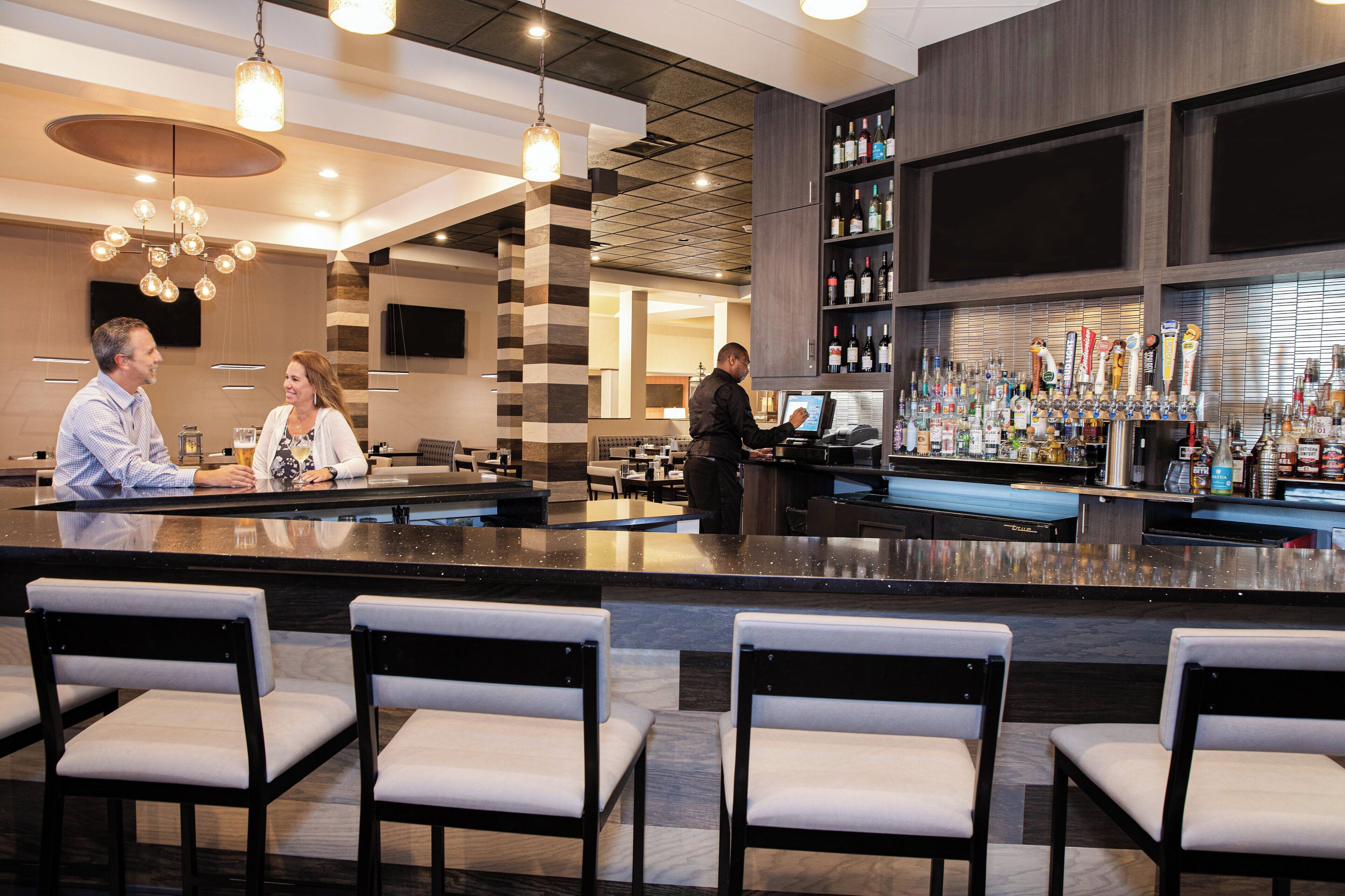A bar area with a bartender, a wine and liquor display, and seating.