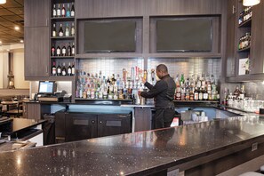 A bar area with a bartender preparing drinks, shelves stocked with bottles, and a computer monitor on the counter. - Holiday Inn St. Louis Arpt West-Earth City by IHG (Earth City)
