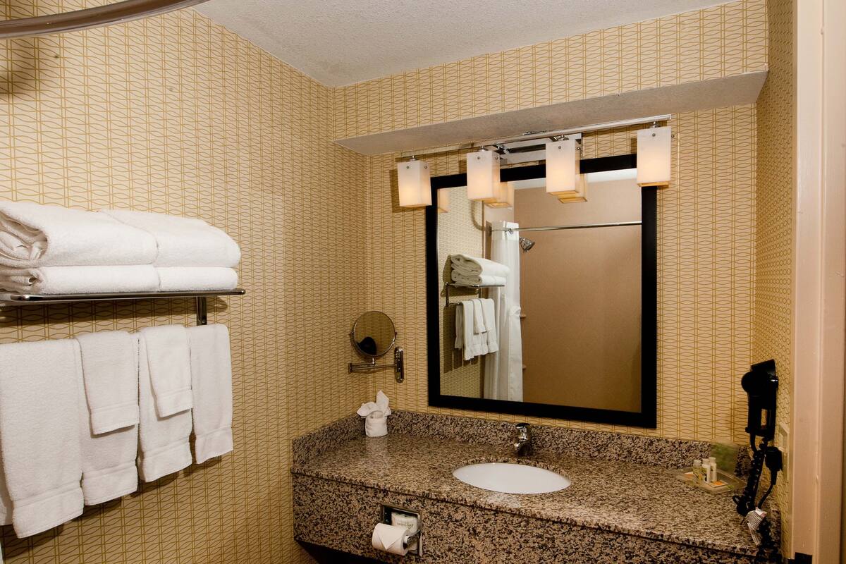 A bathroom with a granite countertop, a sink, a mirror, and a towel rack with folded towels.