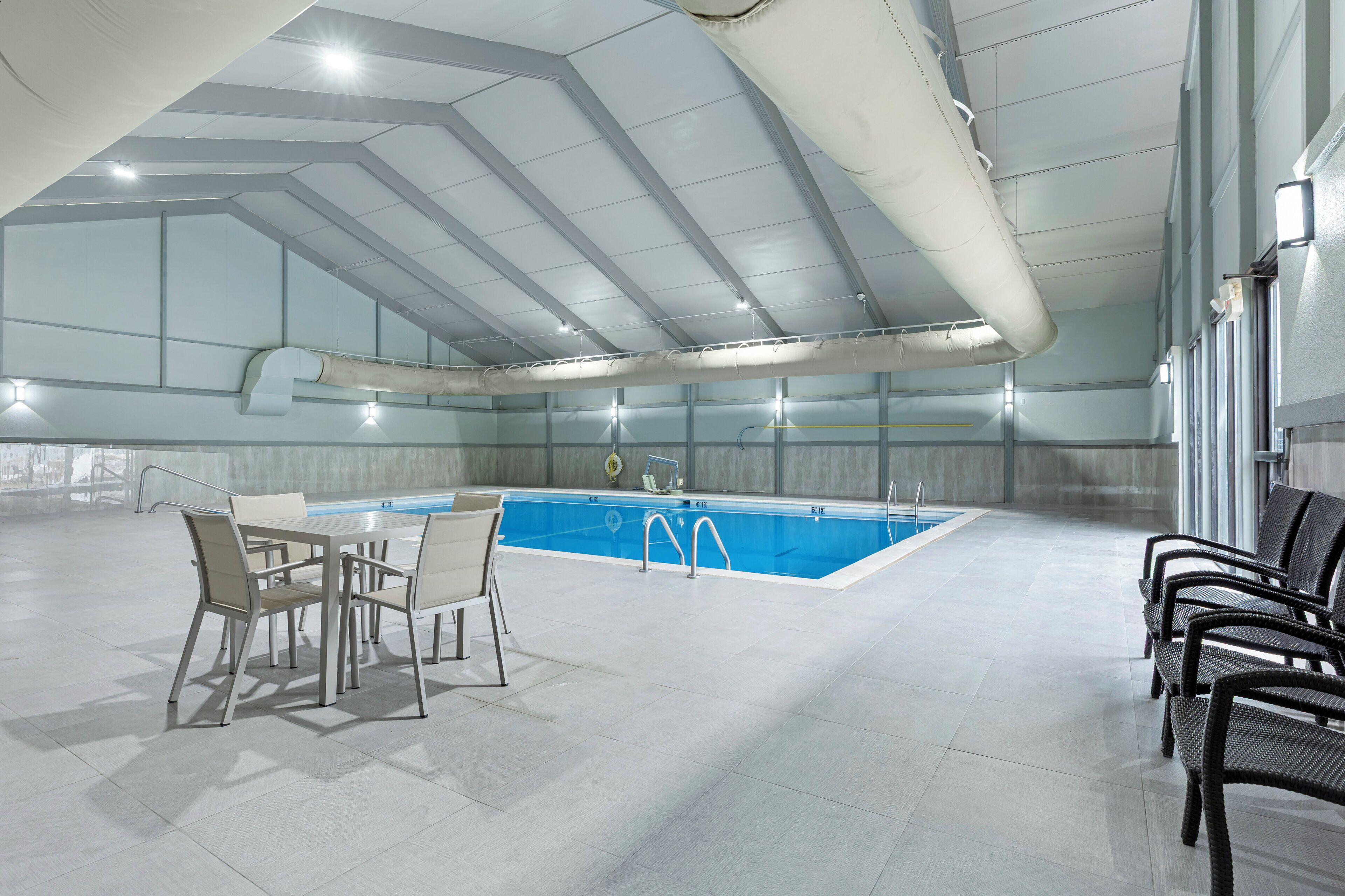 An indoor swimming pool with a tiled floor, a pool table, and seating areas.