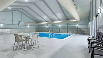 An indoor swimming pool with a tiled floor, a pool table, and seating areas.