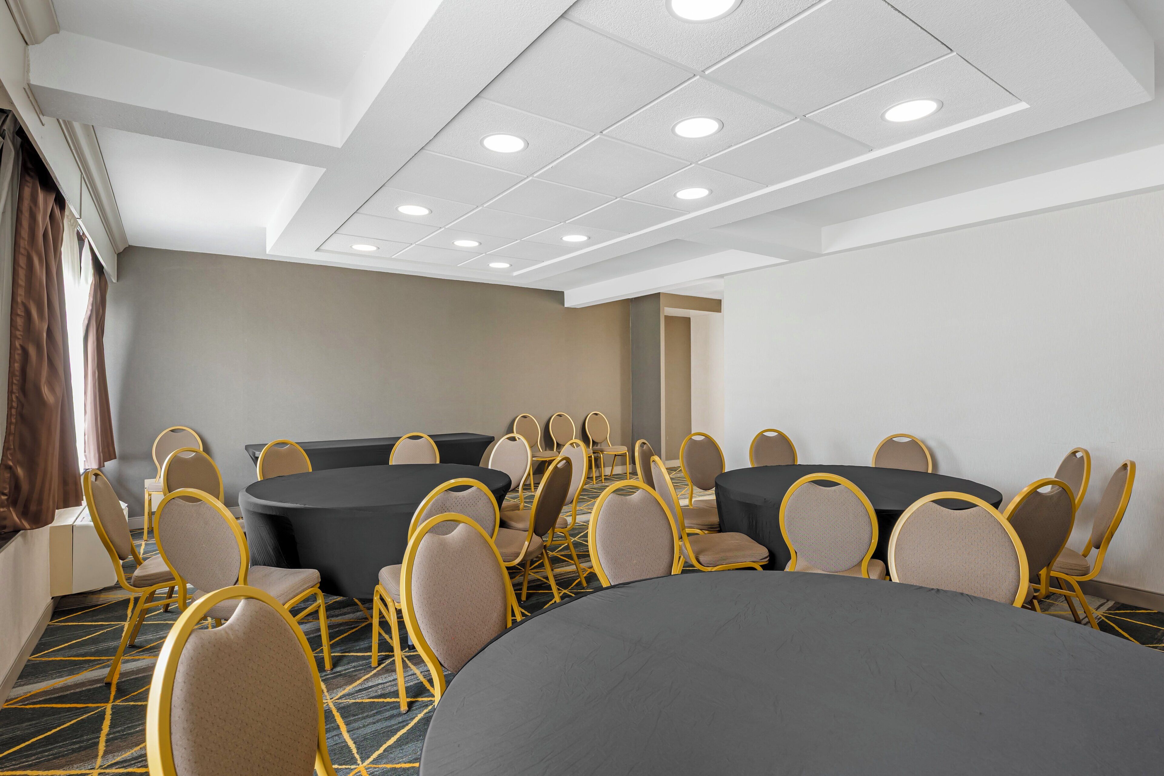 A conference room with round tables and chairs, a carpeted floor, and a white ceiling with recessed lighting.