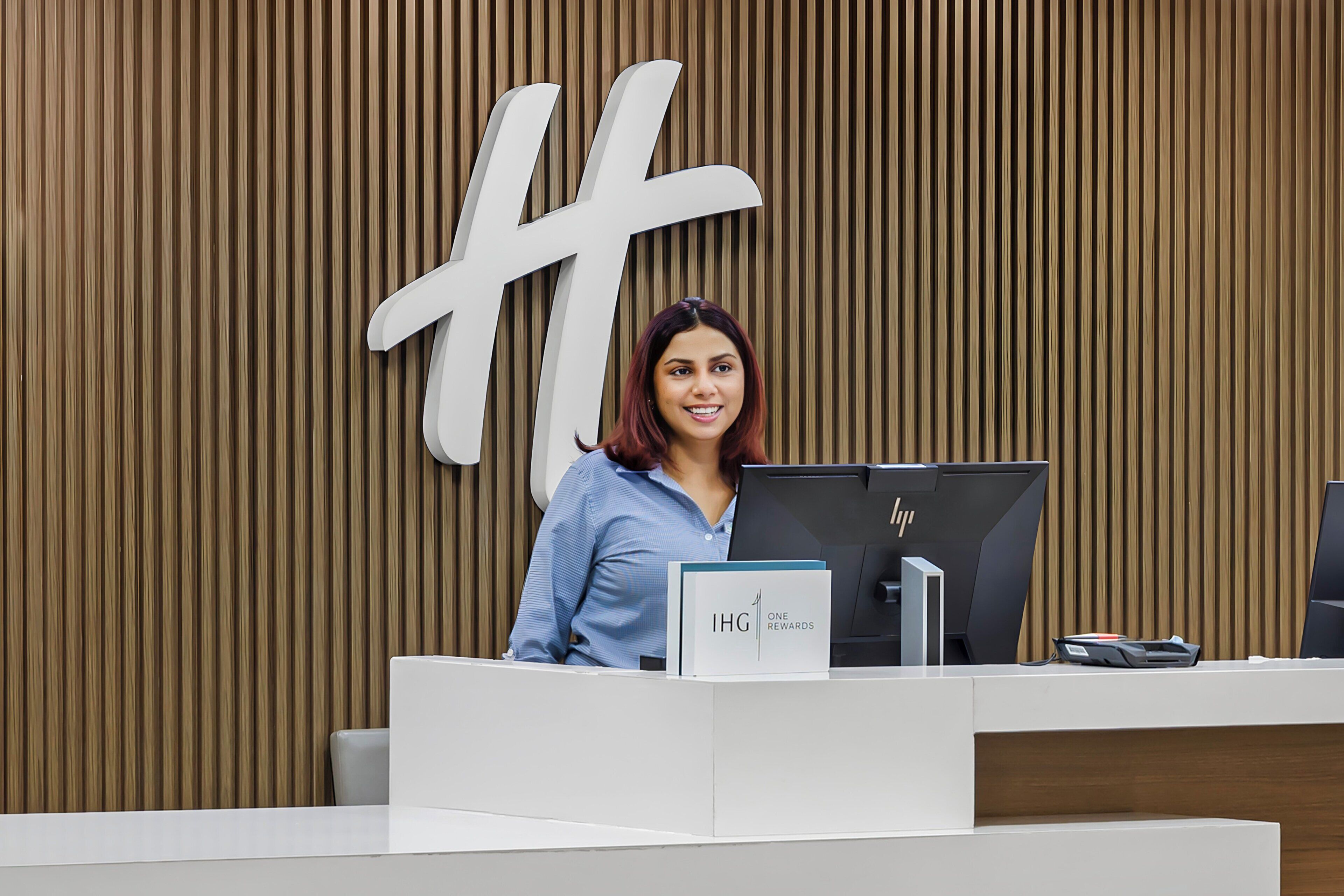 A reception desk with a large logo, a computer, and a sign that reads 'IHG ONE REWARDS'.