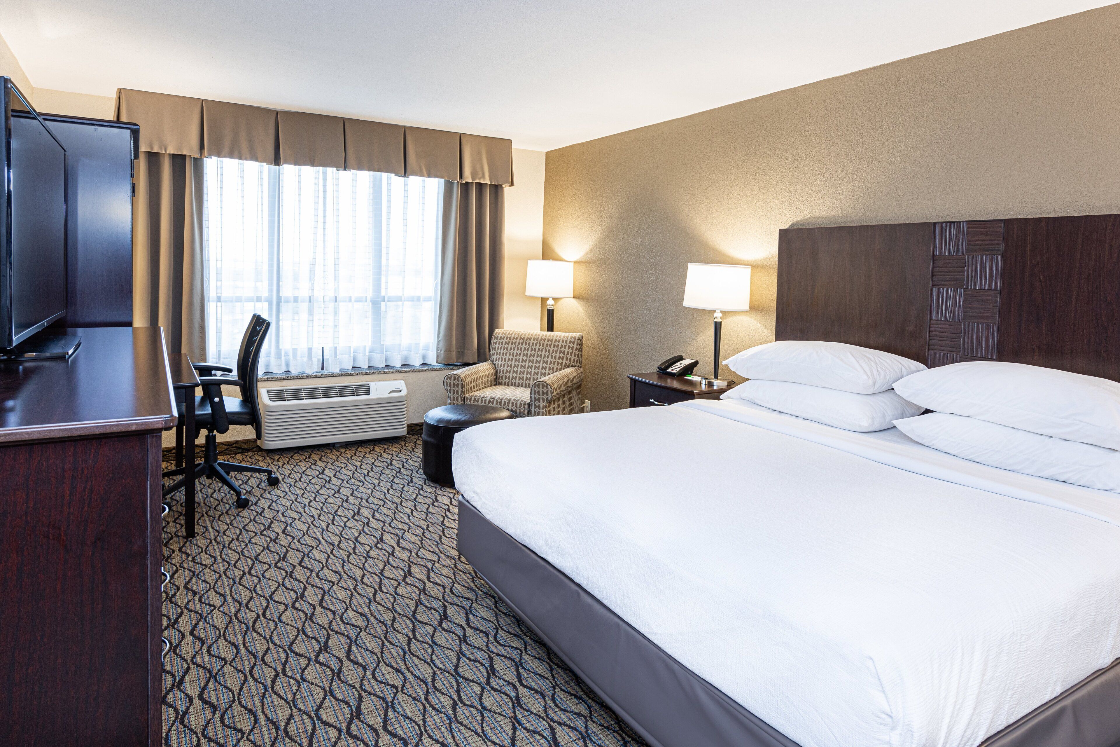 A hotel room with a large bed, a desk with a chair, a television, and a window with curtains.