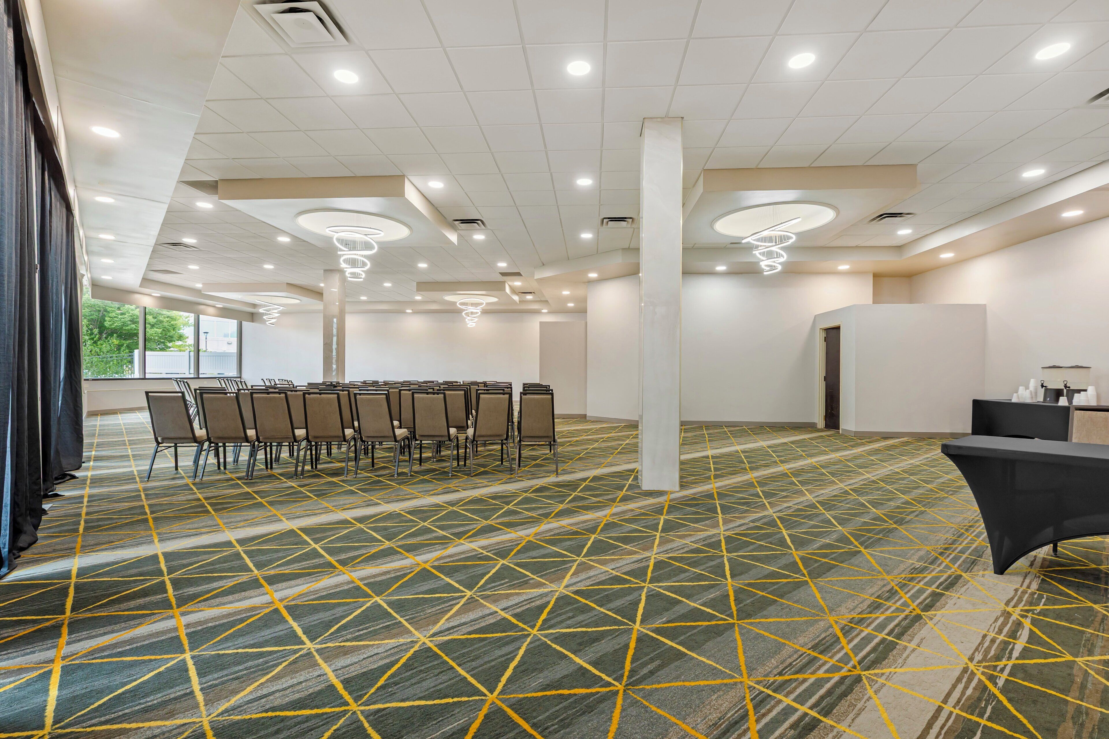 A conference room with a geometric patterned carpet, rows of chairs, and modern lighting fixtures.