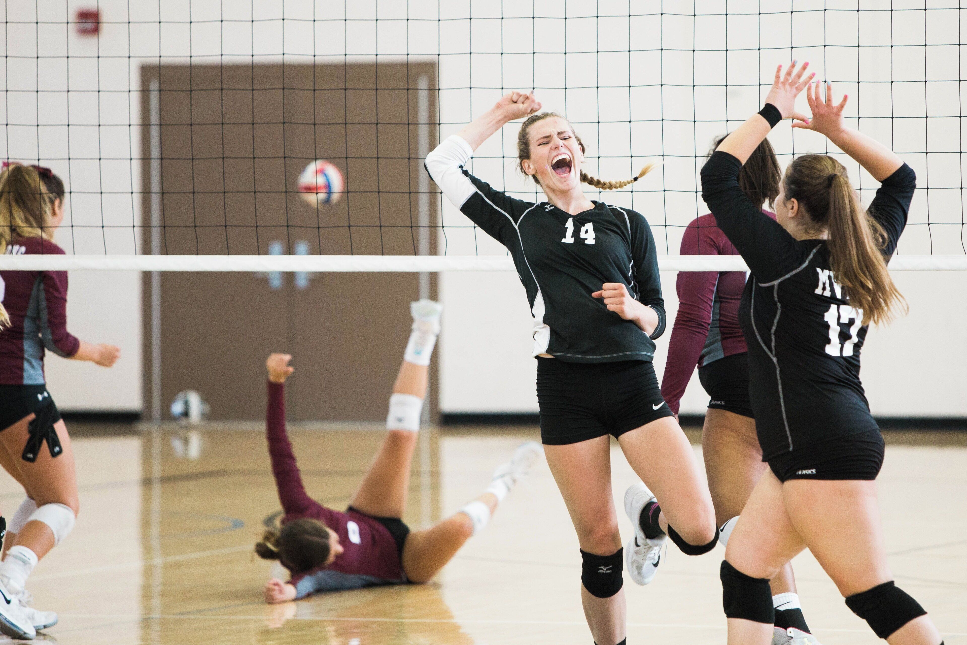 A volleyball game in progress with players in black and maroon uniforms.