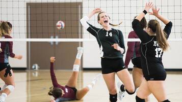A volleyball game in progress with players in black and maroon uniforms.