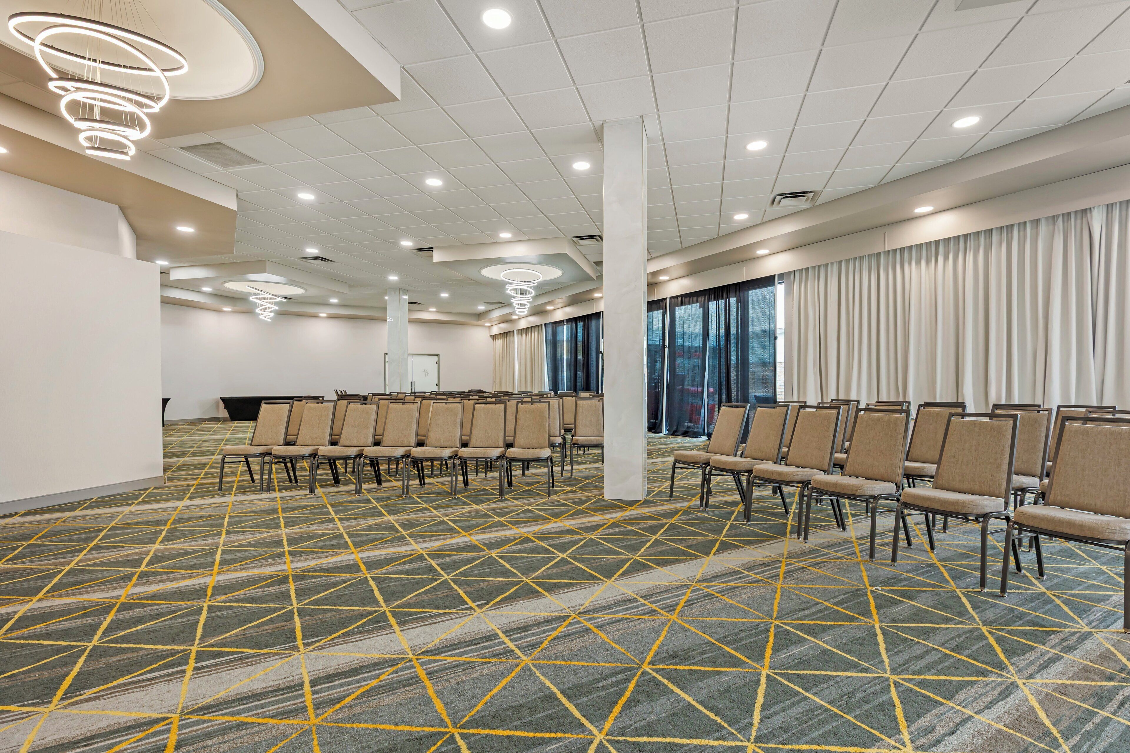 A conference room with rows of chairs, a patterned carpet, and ceiling lights.