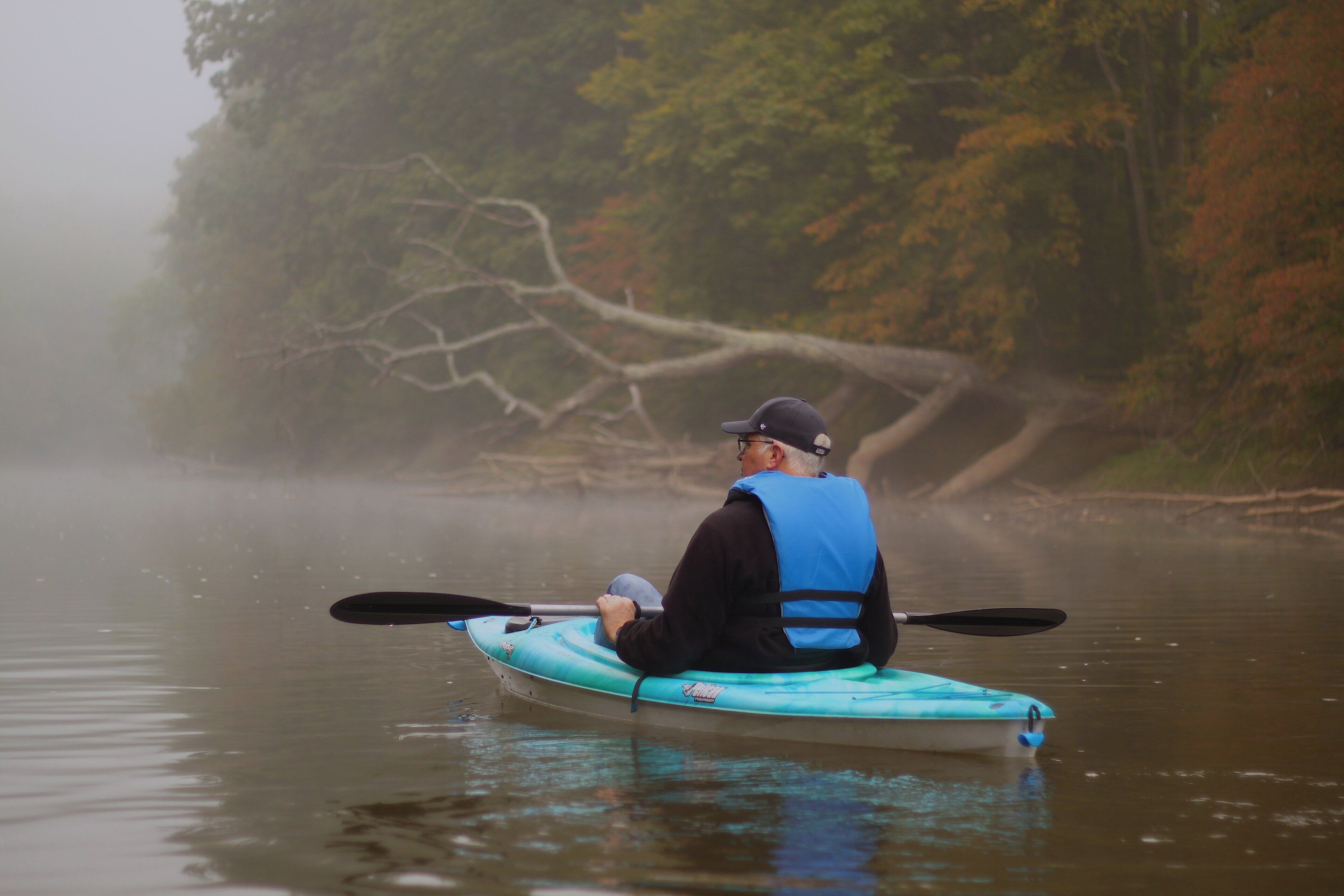 Una persona en kayak en un río tranquilo rodeado de árboles.