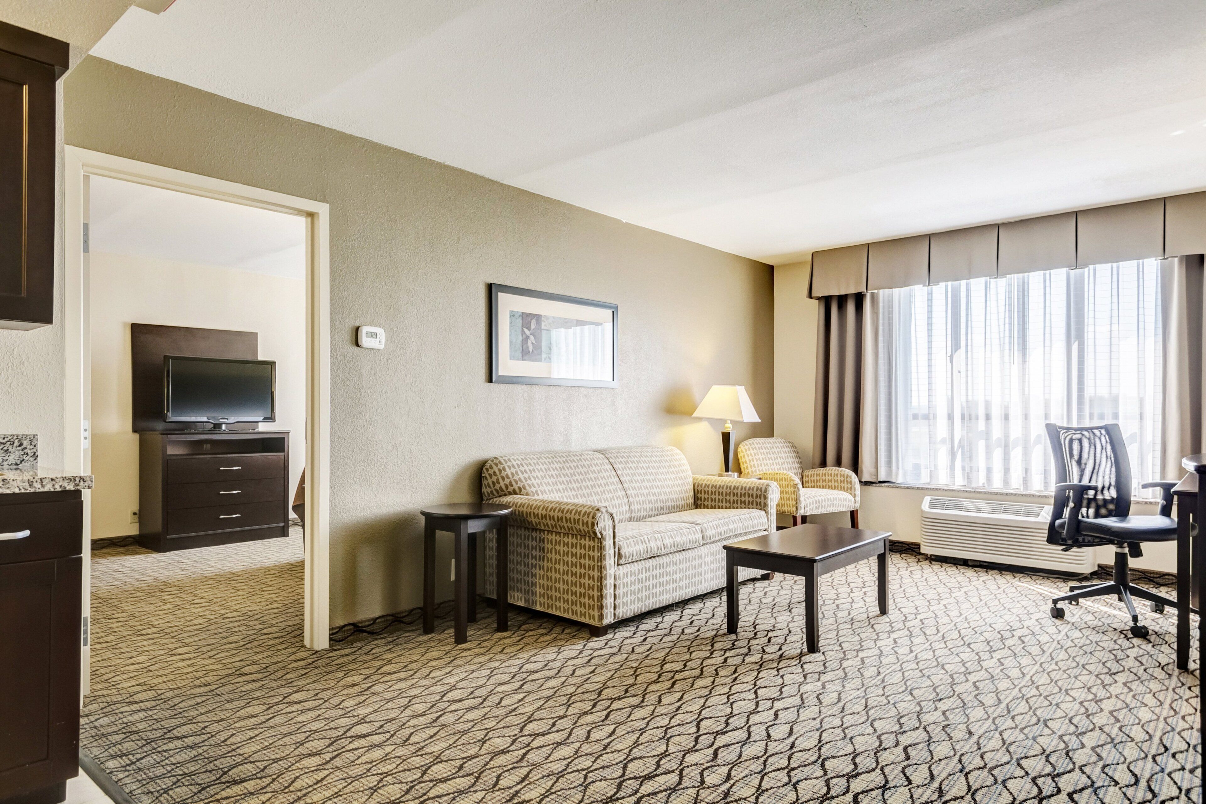 A hotel room with a sofa, a small table, a TV, a lamp, and a chair.