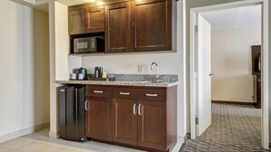 A compact kitchen with dark wooden cabinets, a built-in microwave, and a stainless steel refrigerator.
