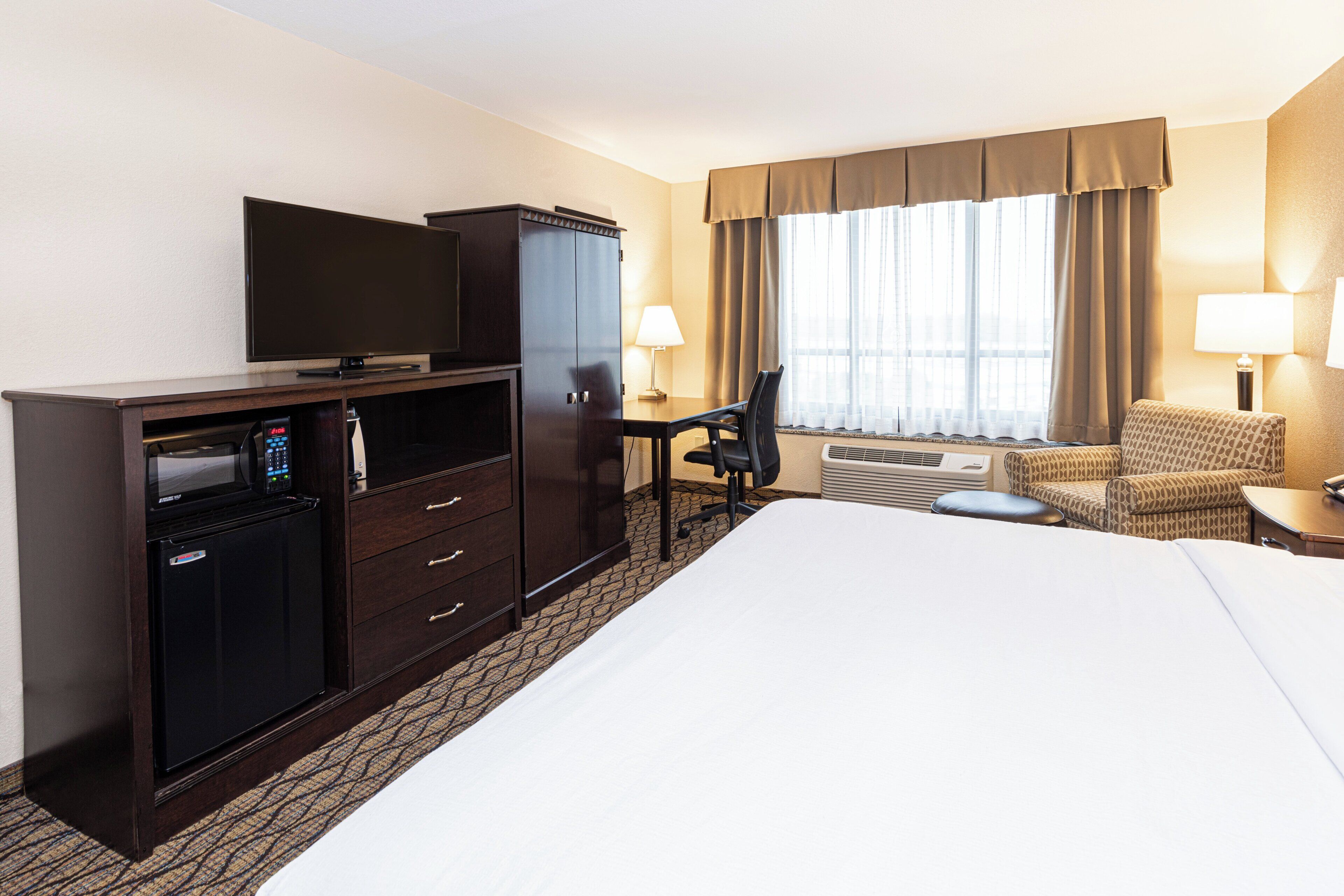 A hotel room with a bed, a TV, a mini-fridge, a desk with a chair, and a sofa.