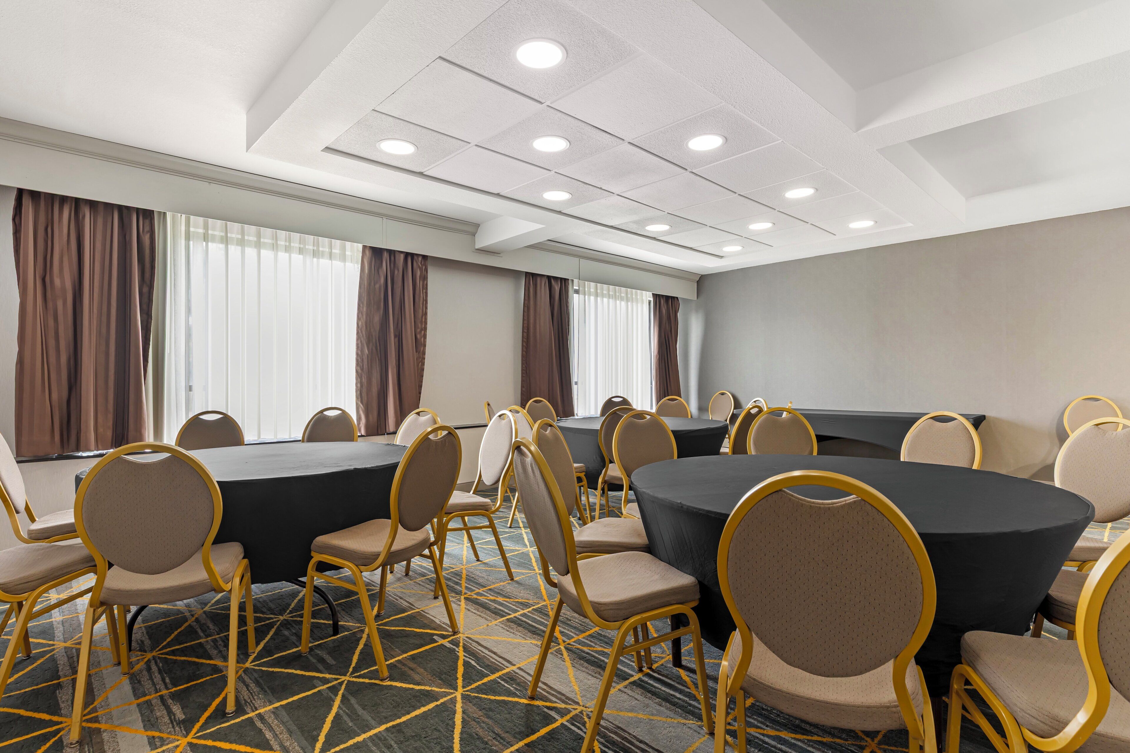 A conference room with round tables, chairs, and a carpeted floor.