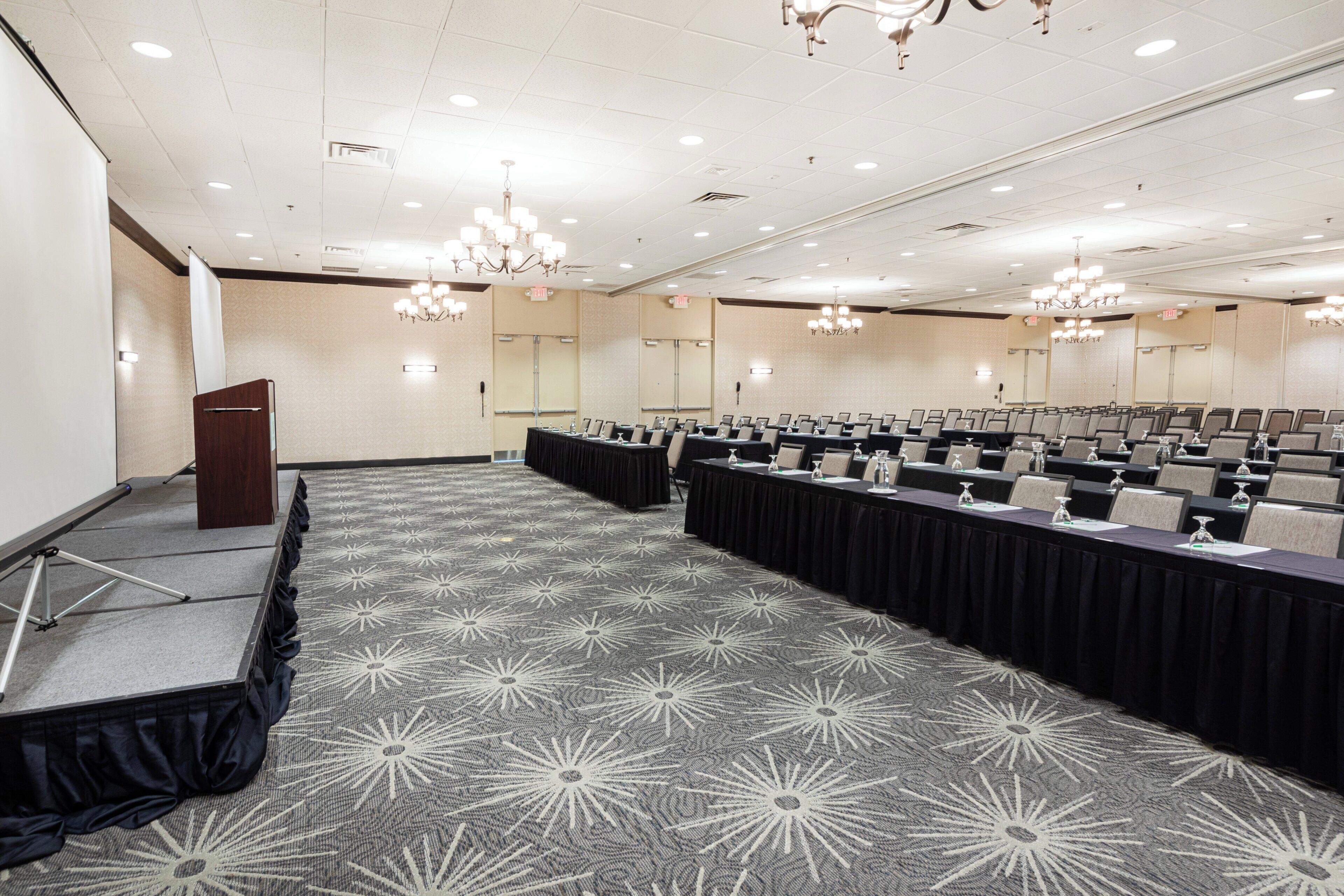 A conference room with a stage, rows of tables, and chandeliers.