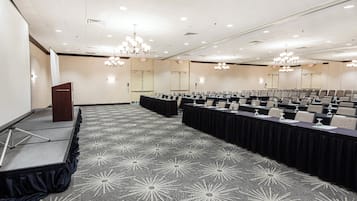 A conference room with a stage, rows of tables, and chandeliers.