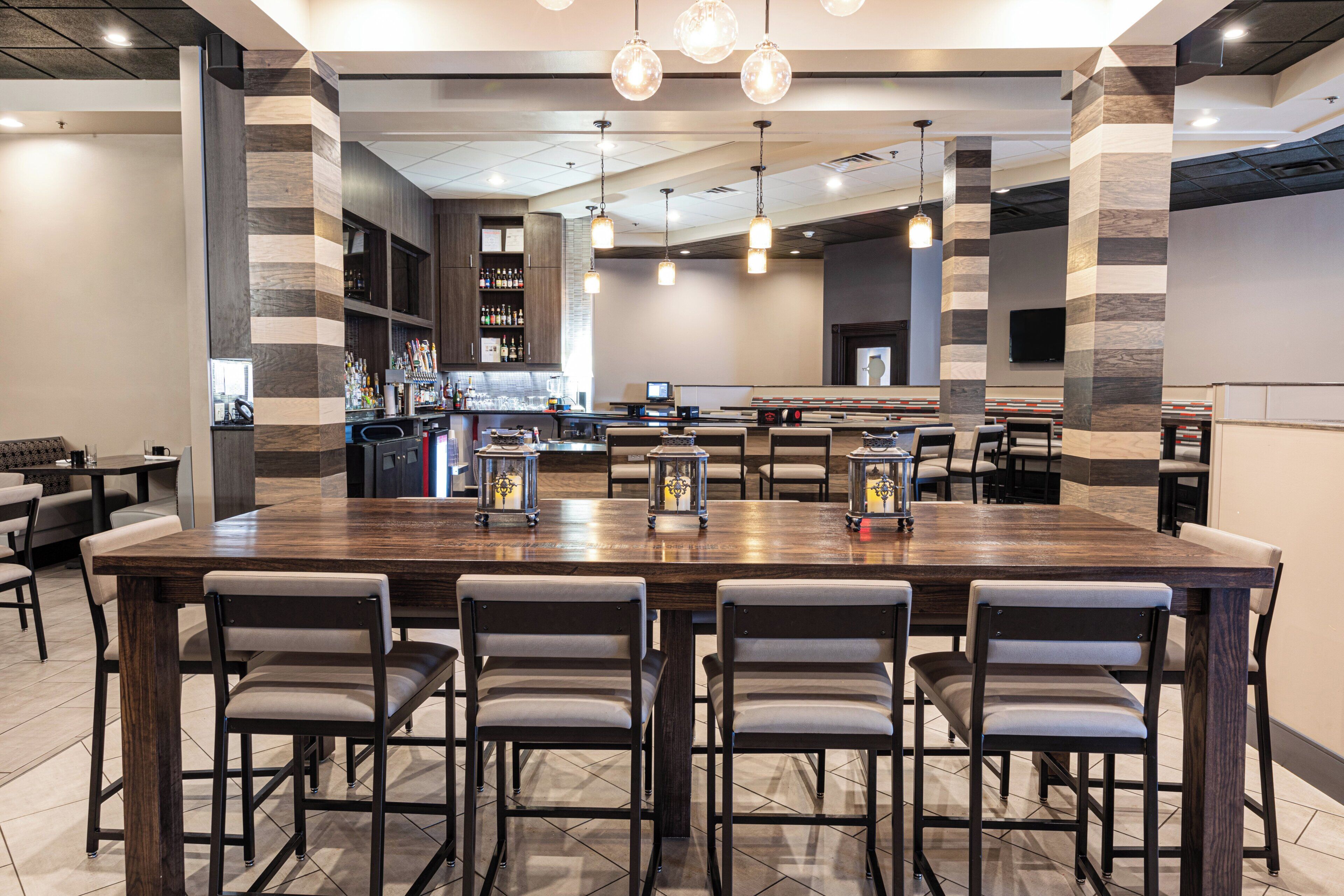 A spacious bar area with a long wooden counter, multiple bar stools, and a variety of bar tools.