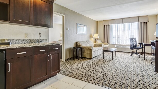A hotel room with a kitchenette, a sofa, a desk, and a large window with curtains.