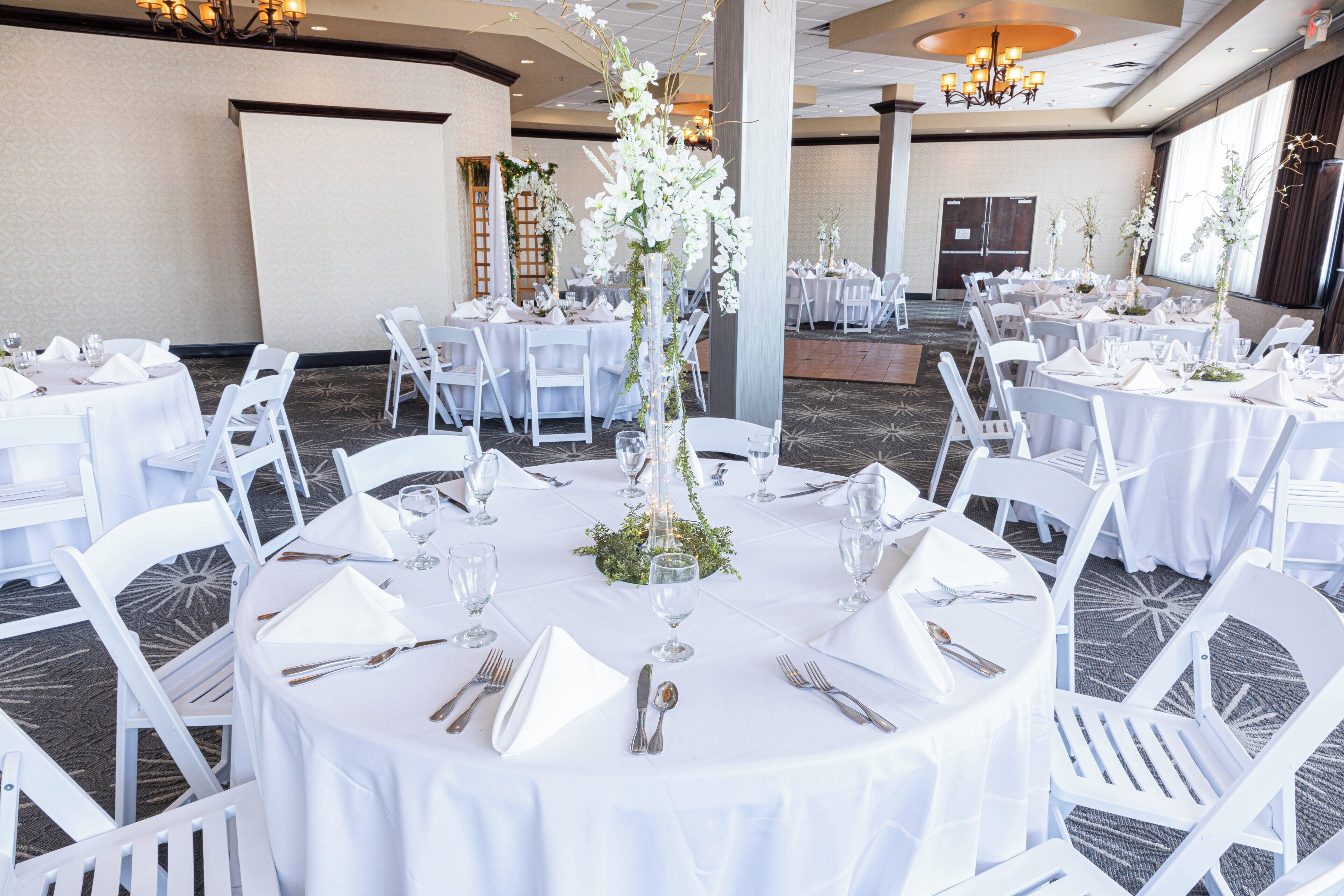 A banquet hall with round tables set for dining, white chairs, and floral centerpieces.