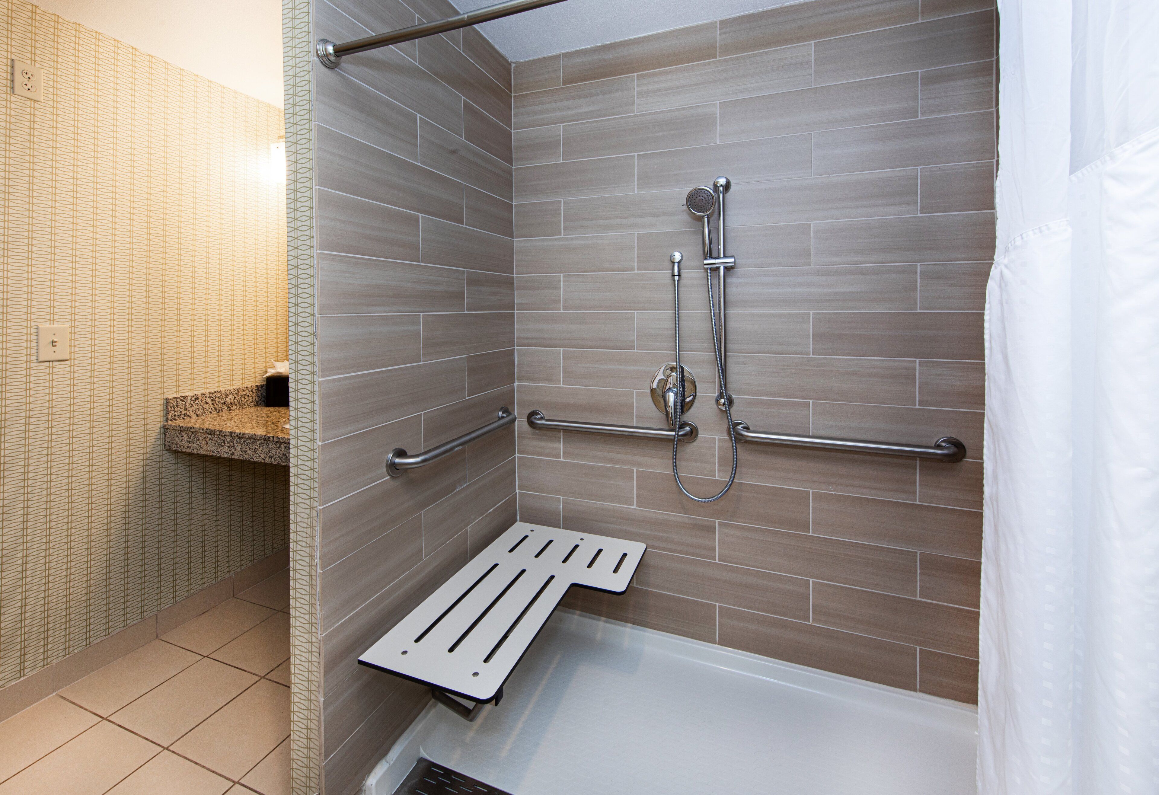 A modern bathroom with a shower, grab bars, and a towel rack.