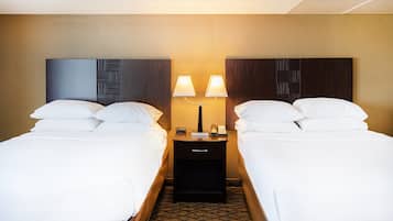 A hotel room with two beds, a nightstand with a lamp, and a phone.