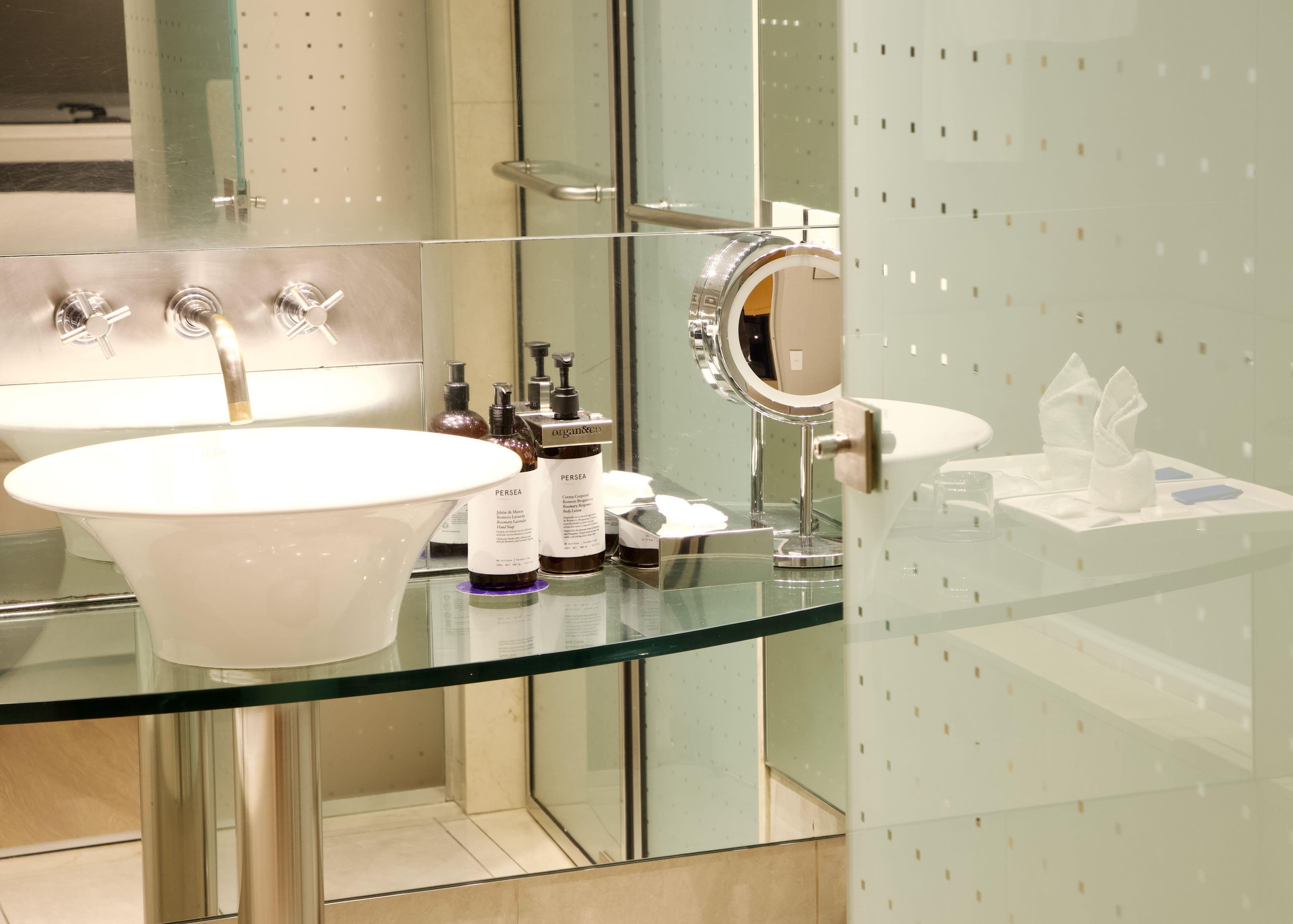Un baño moderno con encimera de vidrio, un lavabo blanco y un espejo.