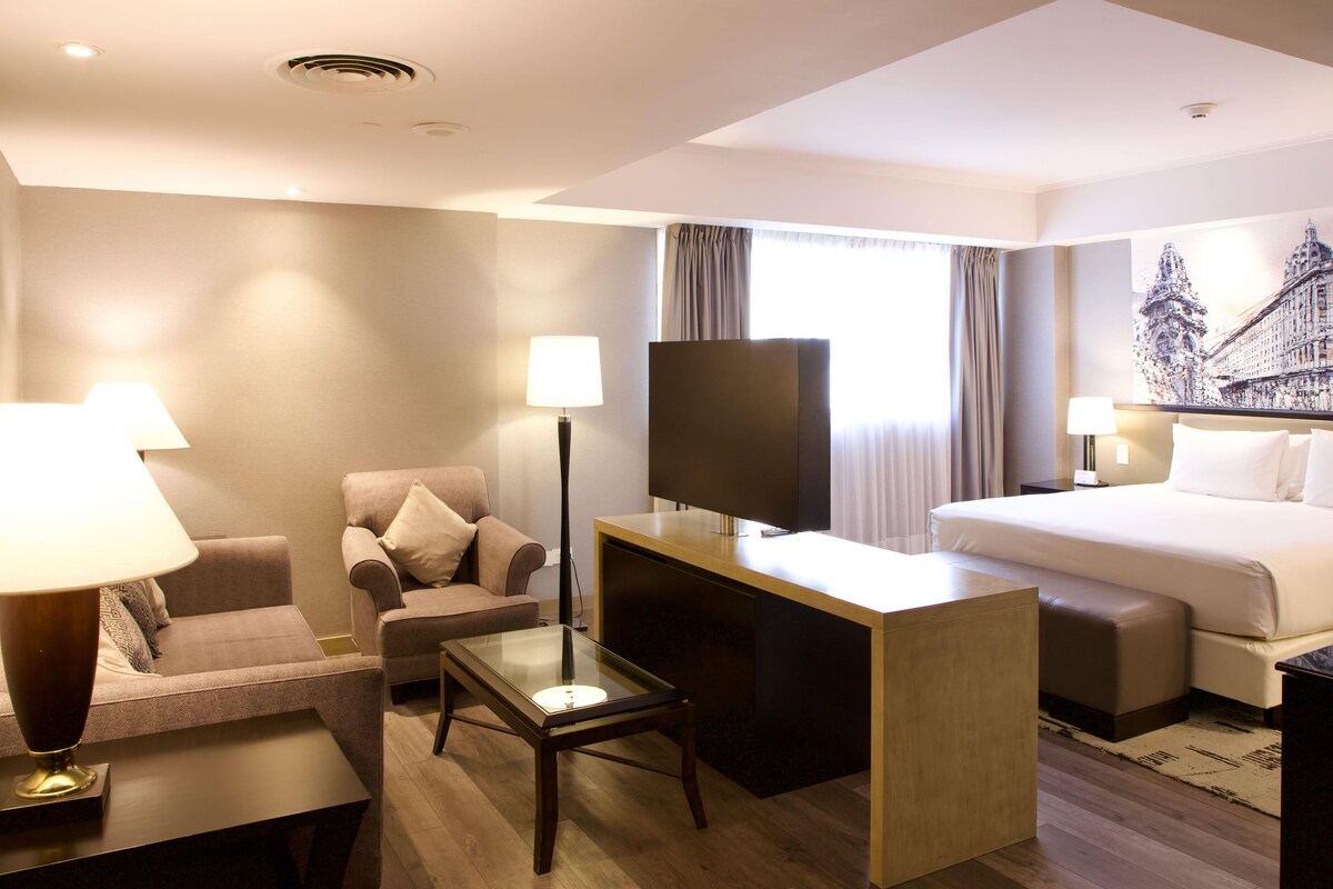 Een hotelkamer met een bed, een bureau, een stoel, een televisie en een lamp.