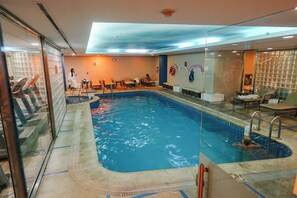 En indendørs swimmingpool med klart vand, glasvægge og flisegulv.