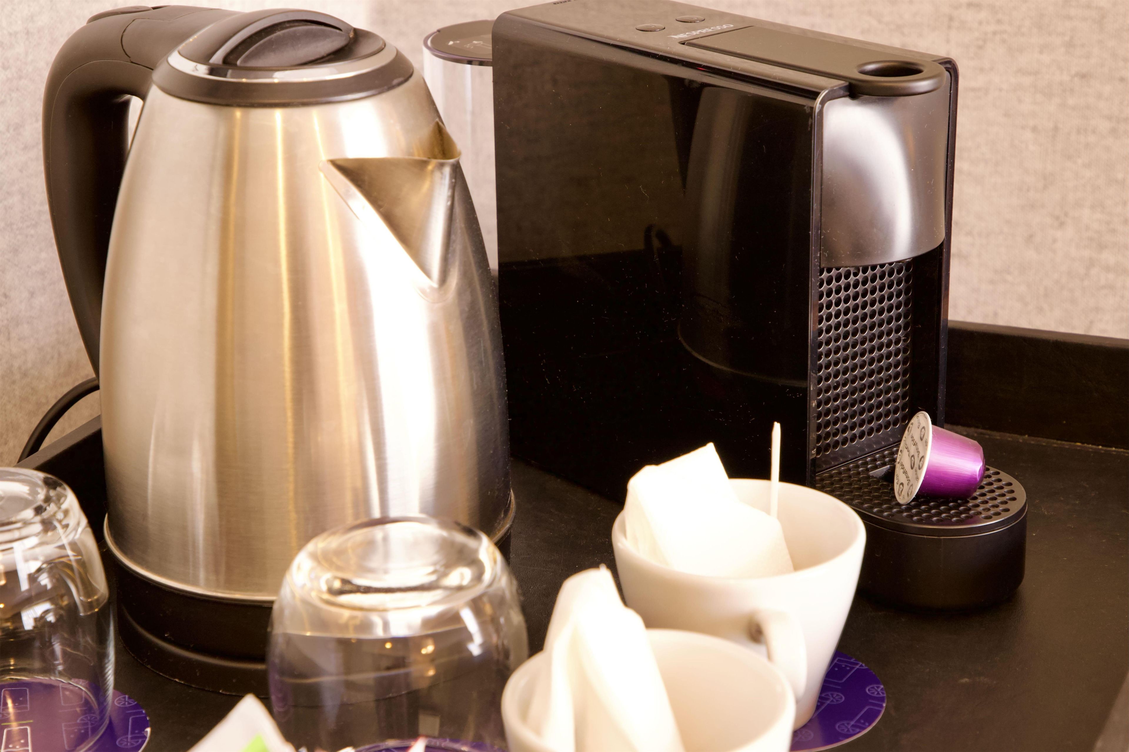 Un coin cuisine équipé d’une bouilloire, d’une machine à café, de tasses et d’un verre.