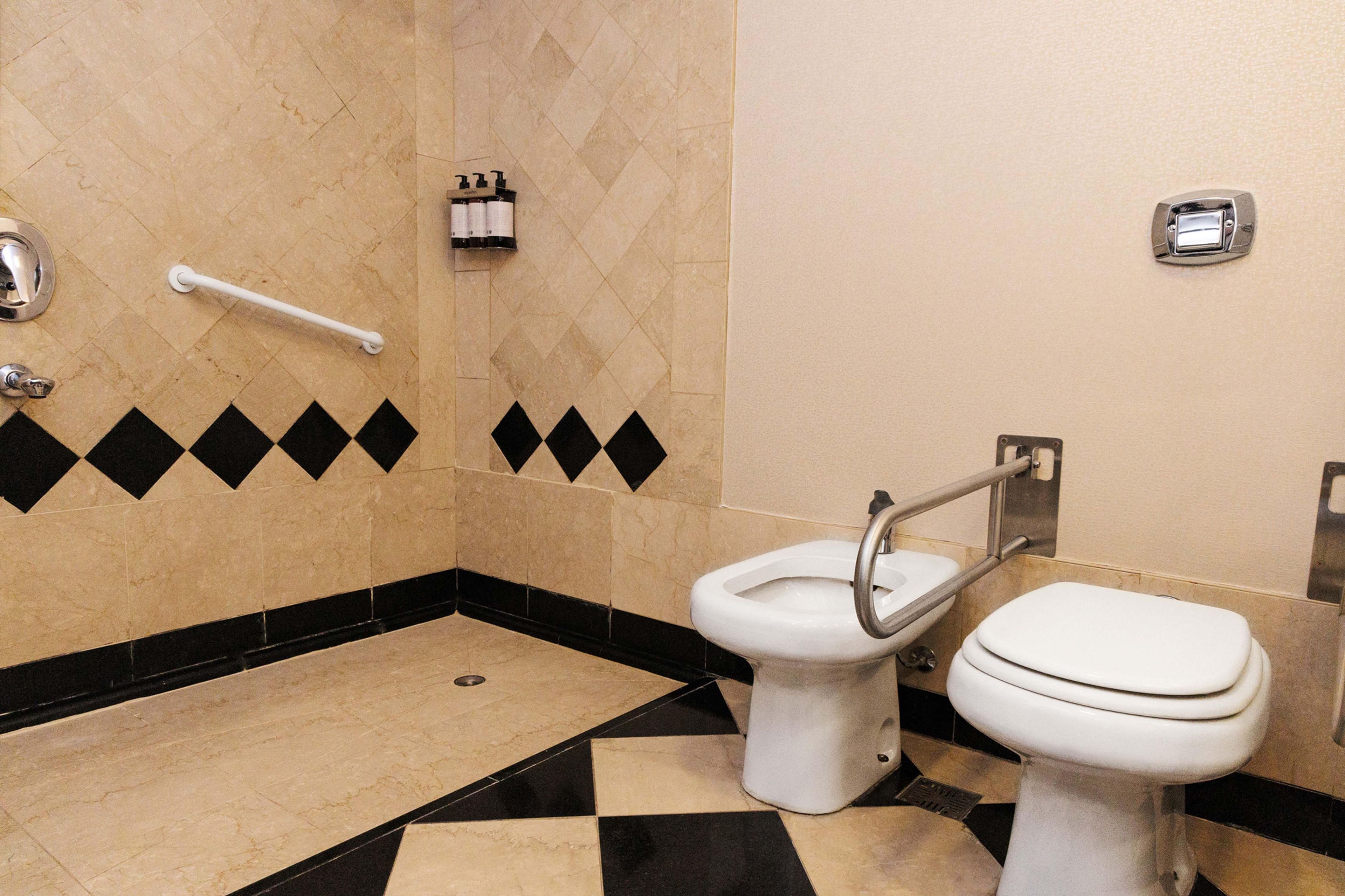 Baño con inodoro, bidé y barras de apoyo.