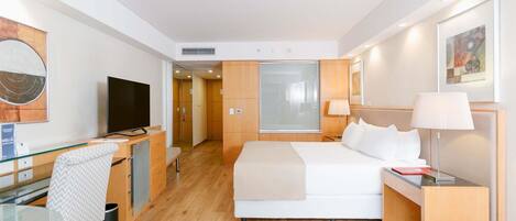 A hotel room with a bed, bedside table, lamp, TV, desk, chair, and a mirror.