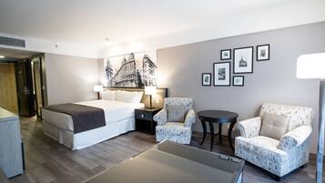 A hotel room with a bed, two armchairs, a small table, and a wall with framed pictures.
