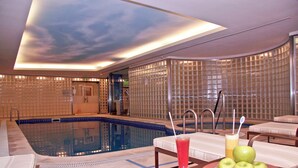A modern indoor pool area with a glass wall, lounge chairs, and a table with a drink and apples. - DoubleTree by Hilton Buenos Aires (Buenos Aires)