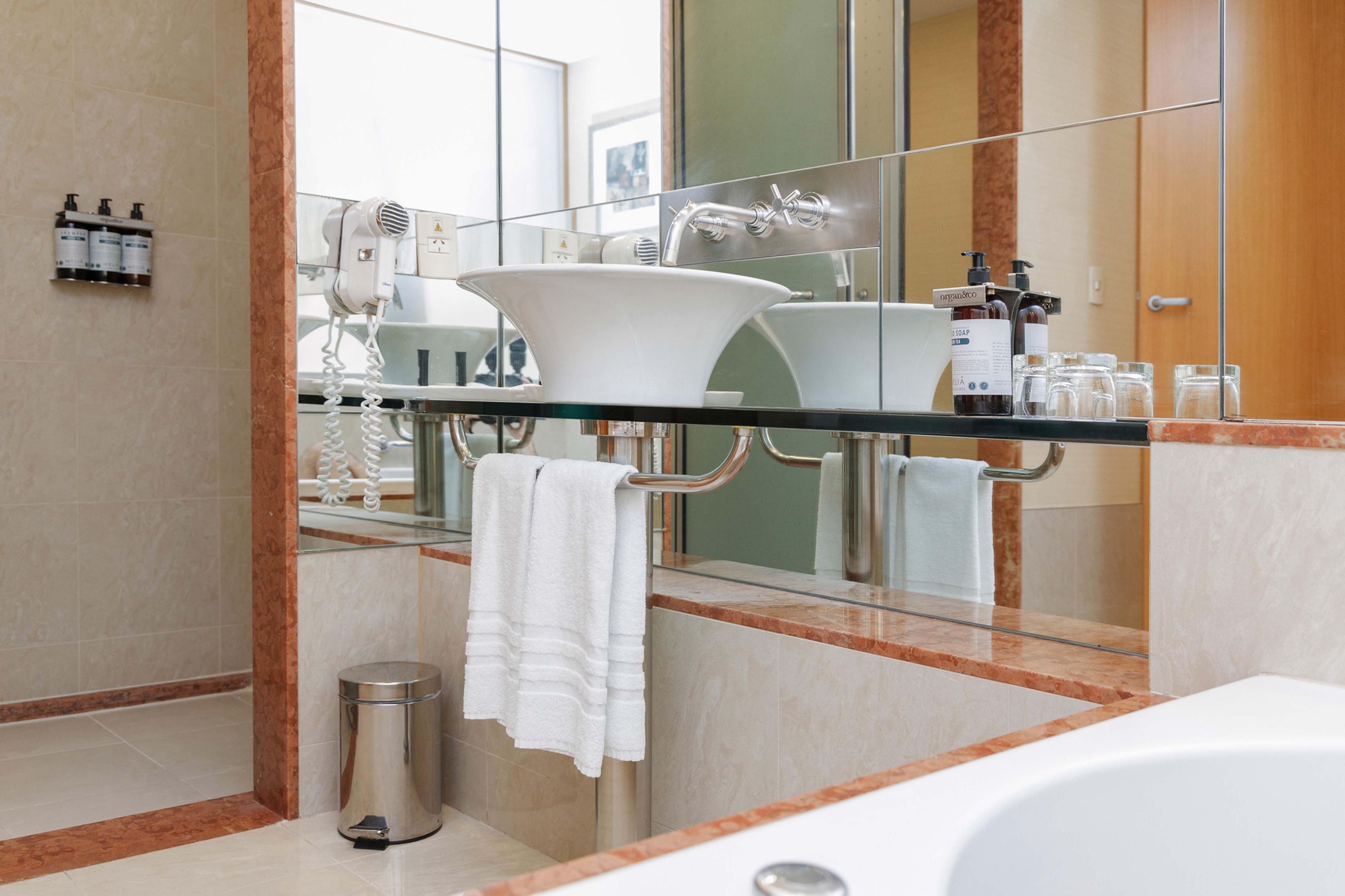 A modern bathroom with a glass partition, a white sink, a large mirror, and a white bathtub.