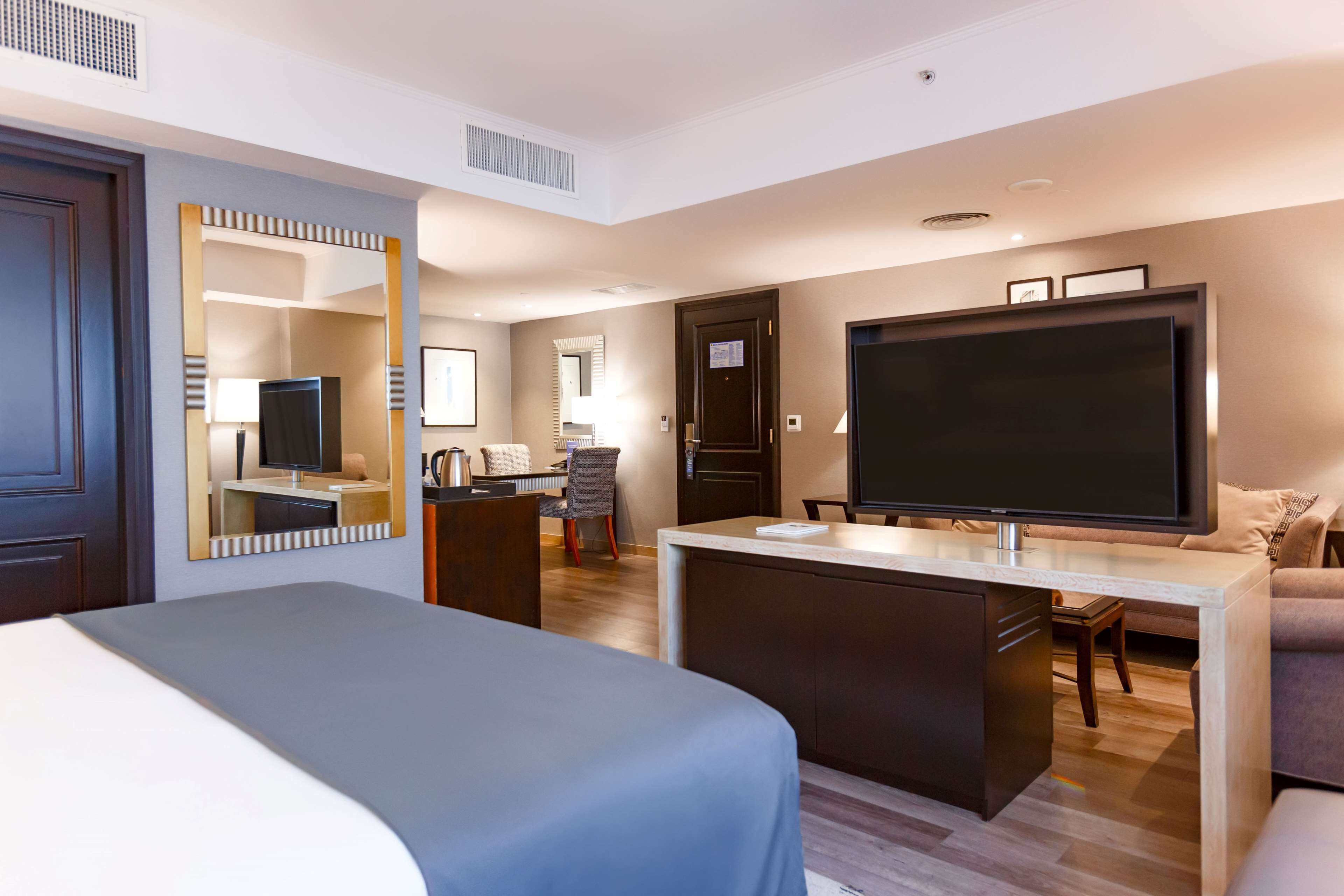 A hotel room with a bed, a desk, a television, a mirror, and a seating area with a couch and chairs.